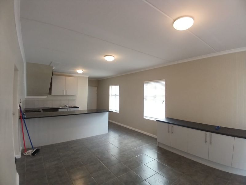 Spacious open-plan living and kitchen area featuring neutral cabinetry, dark countertops, tiled flooring, and ample natural light through multiple windows.
