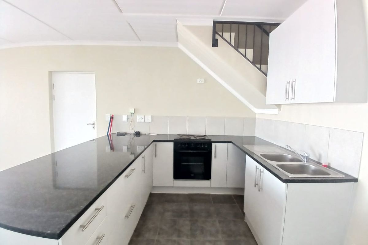A clean, functional kitchen featuring white cabinetry, dark granite countertops, a built-in oven and hob, and a double basin sink, located beneath a staircase.