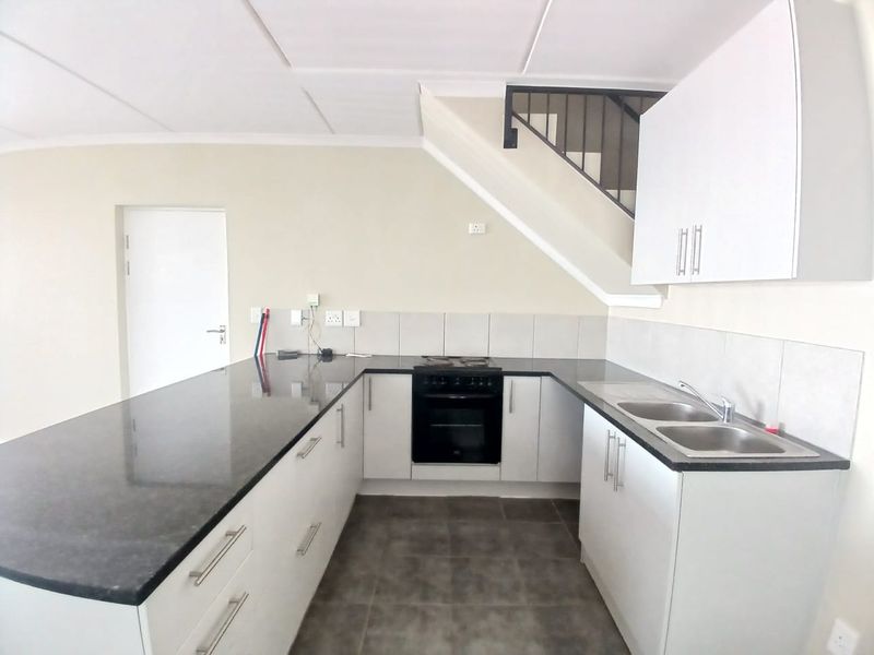 A clean, functional kitchen featuring white cabinetry, dark granite countertops, a built-in oven and hob, and a double basin sink, located beneath a staircase.