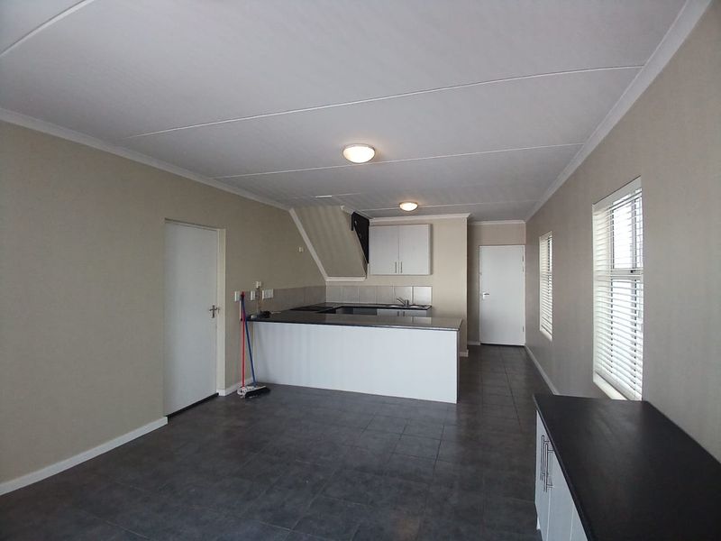 An open-plan living and kitchen area featuring tiled flooring, neutral walls, and a functional kitchen island with built-in cabinetry.