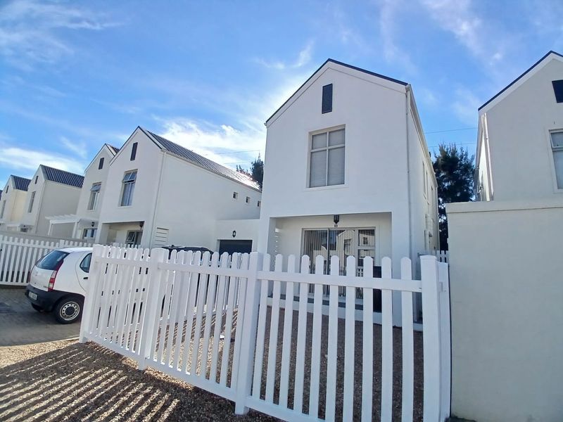 A modern two-story residential home featuring a gabled roofline, white exterior facade, and a secure white picket fence.
