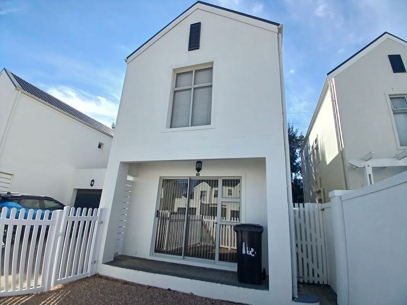 Front elevation of a modern two-story house featuring a gabled roof, white facade, and a paved entrance with a sliding glass door.