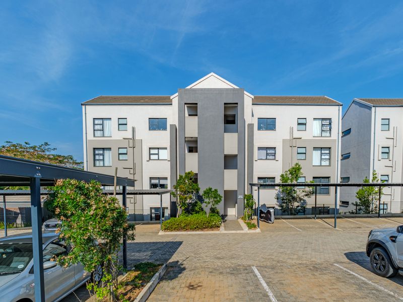 Front elevation of a modern multi-story apartment complex featuring paved parking areas, covered bays, and well-maintained exterior finishes.