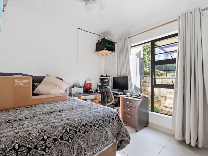 A functional bedroom featuring tiled flooring, a ceiling fan, and a large window providing natural light and garden views.