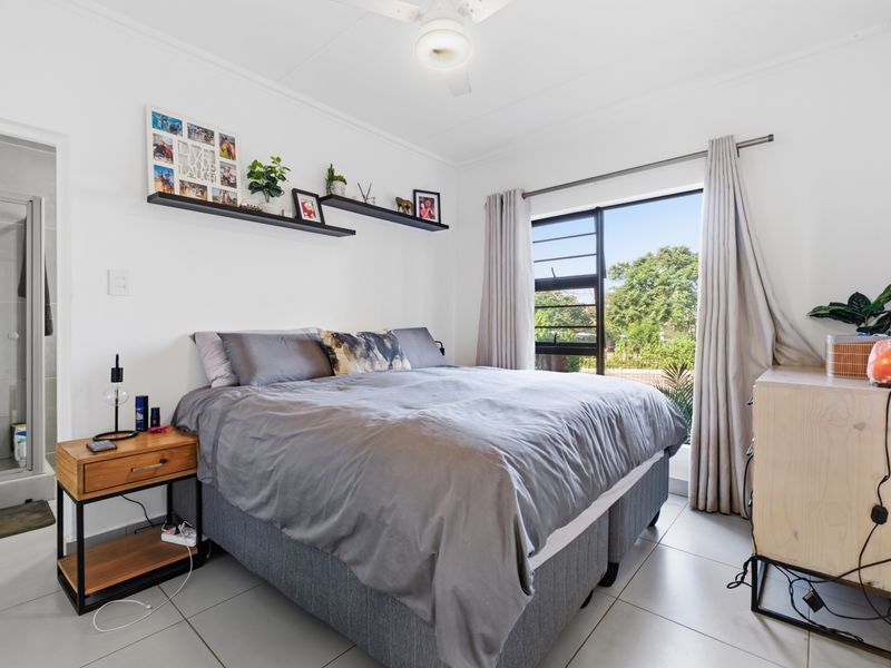A well-lit bedroom featuring tiled flooring, a ceiling fan, and an attached en-suite bathroom with a shower.