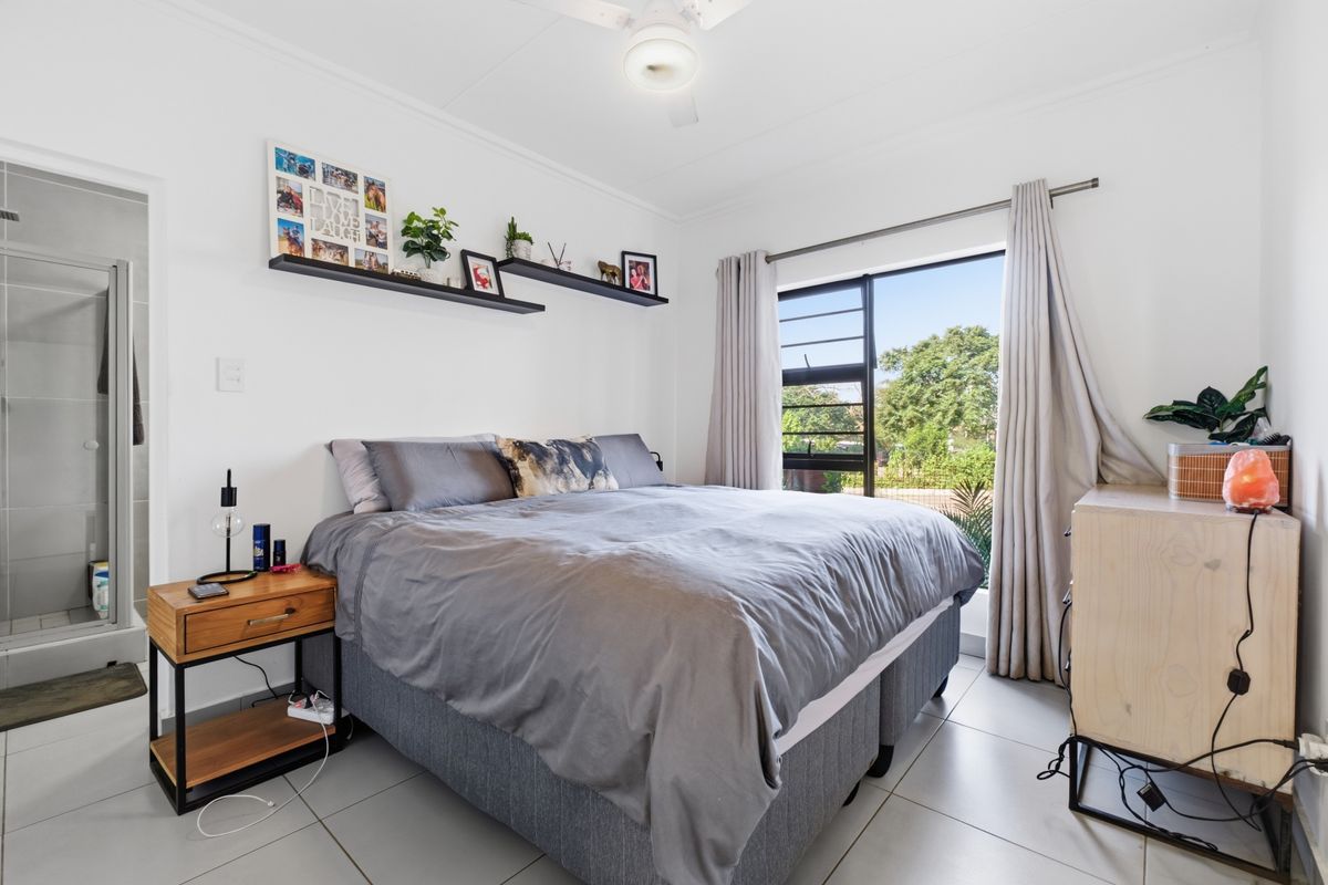 A well-lit bedroom featuring tiled flooring, a ceiling fan, and an attached en-suite bathroom with a shower.
