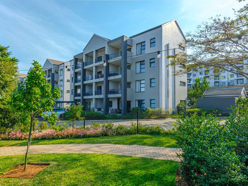 A view of the apartment complex exterior featuring multi-story balconies, a well-maintained garden, and a paved walkway.