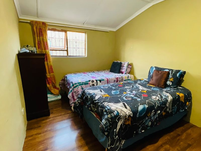 A bedroom featuring laminate flooring, security bars on the window, and ceiling panels. The room requires cosmetic updates to improve its overall condition.