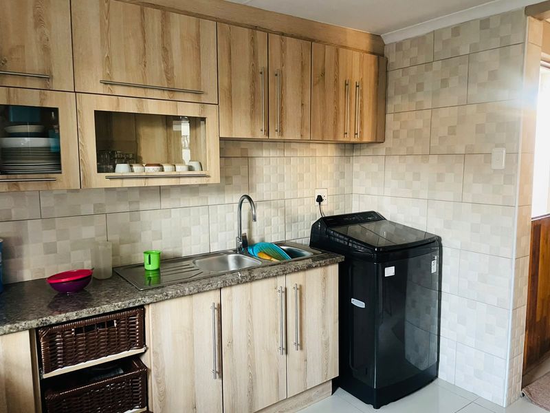 A functional kitchen area featuring light wood-look cabinetry, granite countertops, a stainless steel sink, and neutral tiled backsplash.