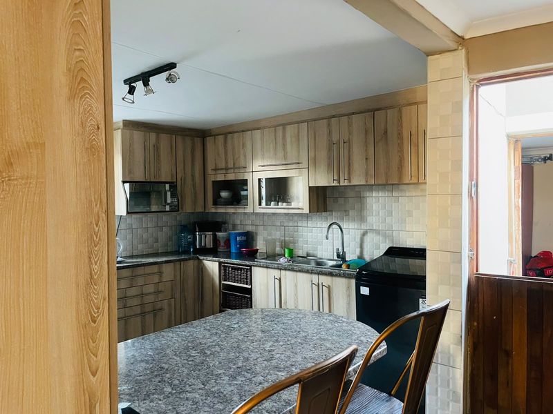 A functional kitchen featuring wood-look laminate cabinetry, granite countertops, a tiled backsplash, and integrated microwave, offering a practical layout for daily meal preparation.