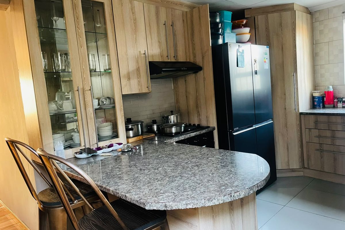 A functional kitchen featuring wood-look cabinetry, granite-style countertops, a breakfast bar, and integrated storage with glass-front display cabinets.