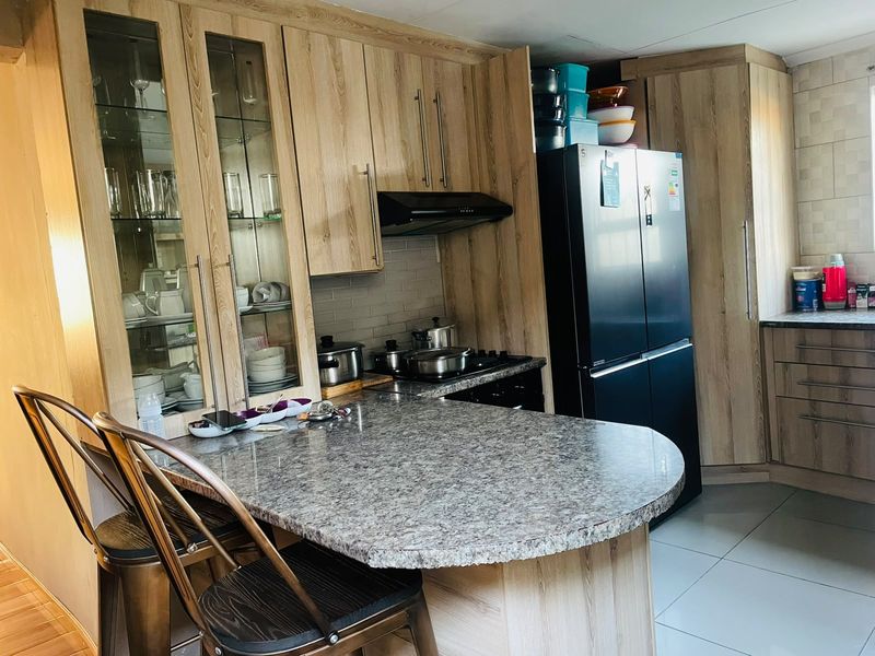 A functional kitchen featuring wood-look cabinetry, granite-style countertops, a breakfast bar, and integrated storage with glass-front display cabinets.