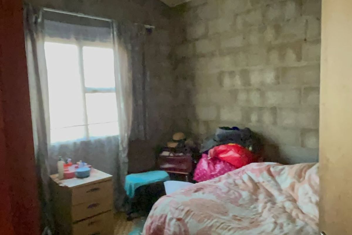 A bedroom featuring exposed concrete block walls and timber roof trusses, requiring cosmetic updates and finishing to improve the overall aesthetic and condition.