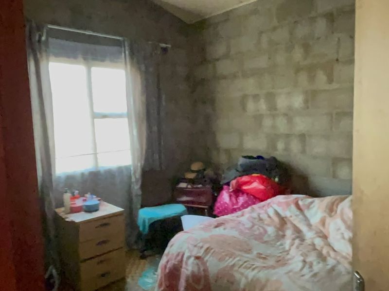 A bedroom featuring exposed concrete block walls and timber roof trusses, requiring cosmetic updates and finishing to improve the overall aesthetic and condition.
