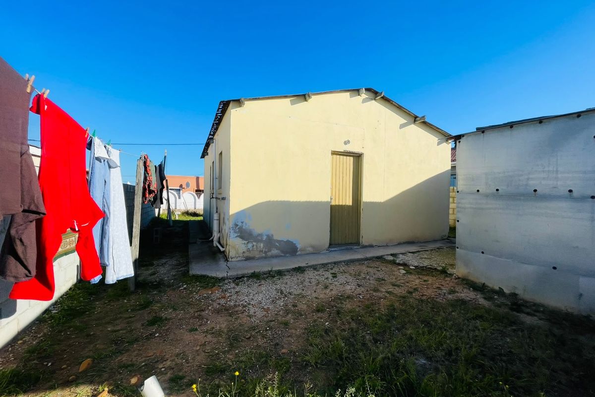 Rear view of a detached residential structure showing plastered walls with visible damp and a concrete apron in need of maintenance.