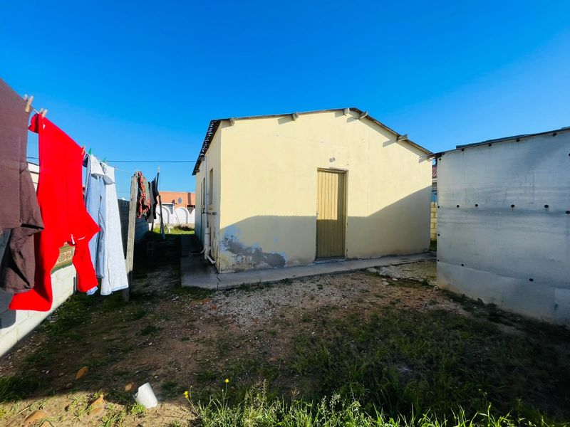 Rear view of a detached residential structure showing plastered walls with visible damp and a concrete apron in need of maintenance.