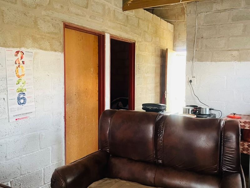 A living area featuring exposed concrete block walls and timber roof trusses, currently in an unfinished state requiring ceiling and wall completion.