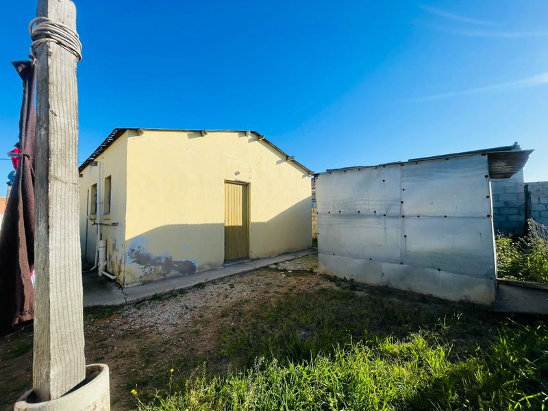 Rear view of the property showing a plastered masonry building and a secondary corrugated metal structure with surrounding yard space.