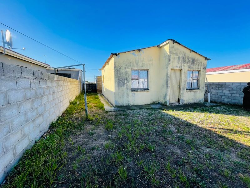 Rear view of a single-story house featuring a concrete block boundary wall and a small yard area requiring maintenance and exterior refurbishment.