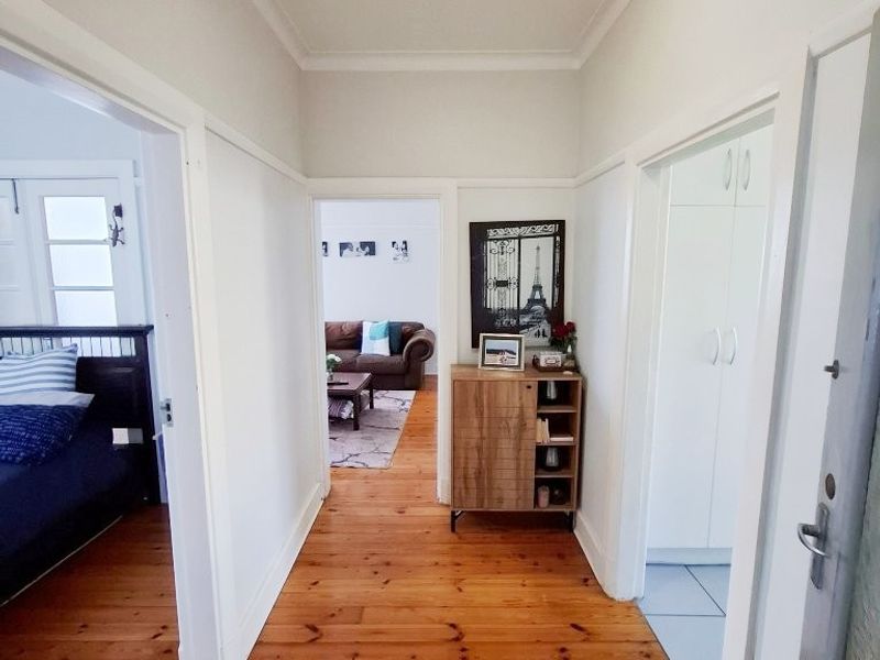 A bright hallway featuring polished timber flooring, classic wainscoting, and built-in storage, providing access to adjacent living and bedroom areas.