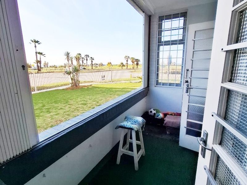 A covered balcony area featuring security bars and a large window overlooking the garden and street.