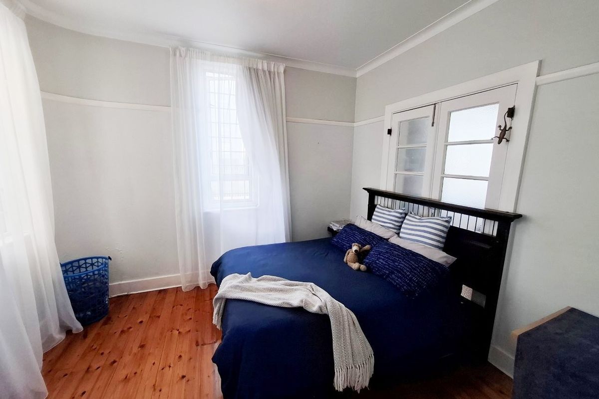 A well-maintained bedroom featuring polished timber flooring, classic picture rails, and charming french doors that provide natural light.