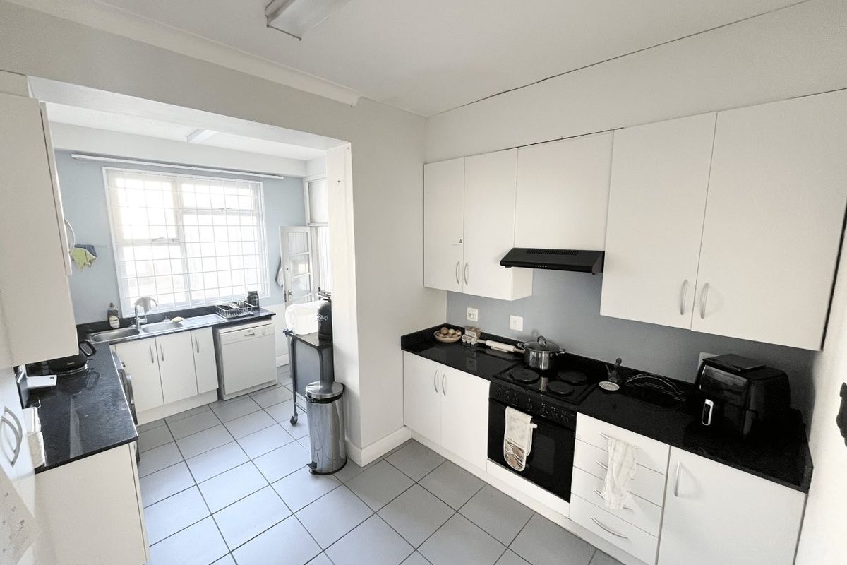 A functional kitchen featuring white cabinetry, black granite countertops, integrated appliances, and tiled flooring, with an adjoining scullery area.
