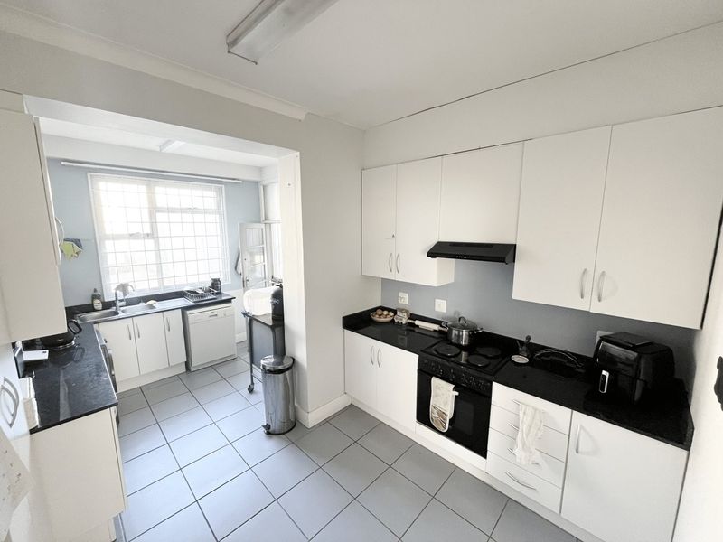 A functional kitchen featuring white cabinetry, black granite countertops, integrated appliances, and tiled flooring, with an adjoining scullery area.