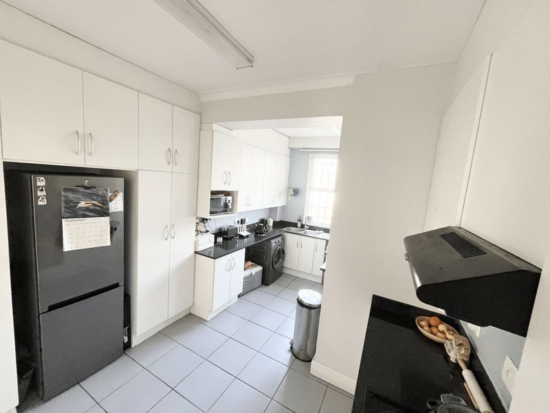A functional kitchen featuring white cabinetry, black granite countertops, tiled flooring, and an integrated extractor fan, providing a clean and practical workspace.