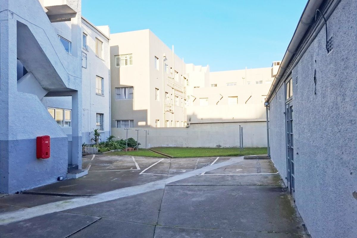 Rear courtyard area of the apartment complex featuring concrete paving, an external staircase, and a small communal garden space.