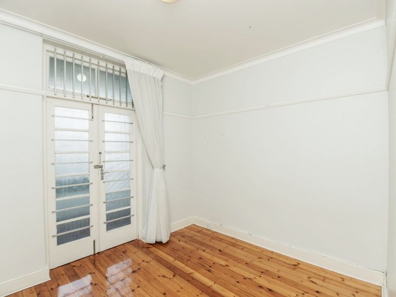 A bright, empty bedroom featuring polished timber flooring, classic picture rails, and double glass panel doors with integrated security bars leading to the exterior.