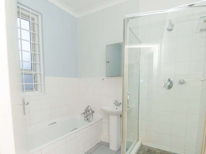 A functional bathroom featuring a pedestal sink, a built-in bathtub, and a separate glass-enclosed shower with tiled finishes.