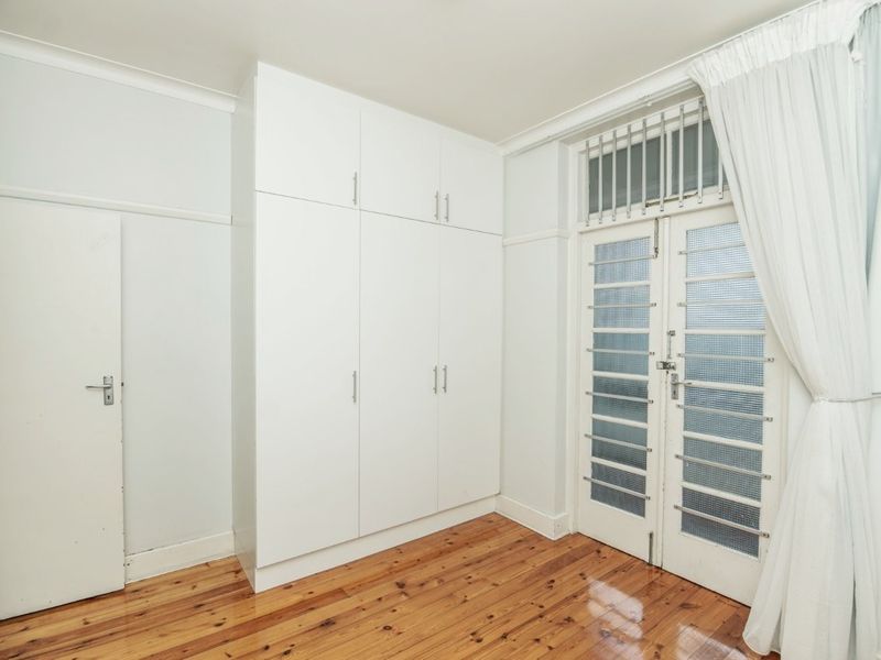A bright, empty bedroom featuring polished timber flooring, ample built-in storage cupboards, and classic french doors leading to an outdoor area.