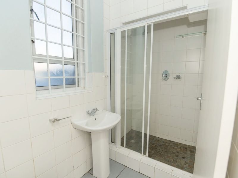 A functional bathroom featuring a pedestal basin, a tiled shower enclosure with a sliding door, and a window with security bars.