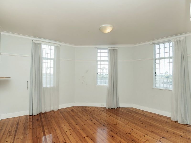 An empty bedroom featuring polished timber flooring, large multi-pane windows with natural light, and classic picture rail detailing.