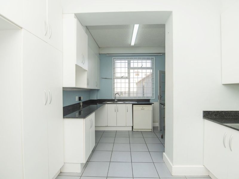 A functional kitchen featuring white built-in cabinetry, dark granite countertops, tiled flooring, and a window with security bars.