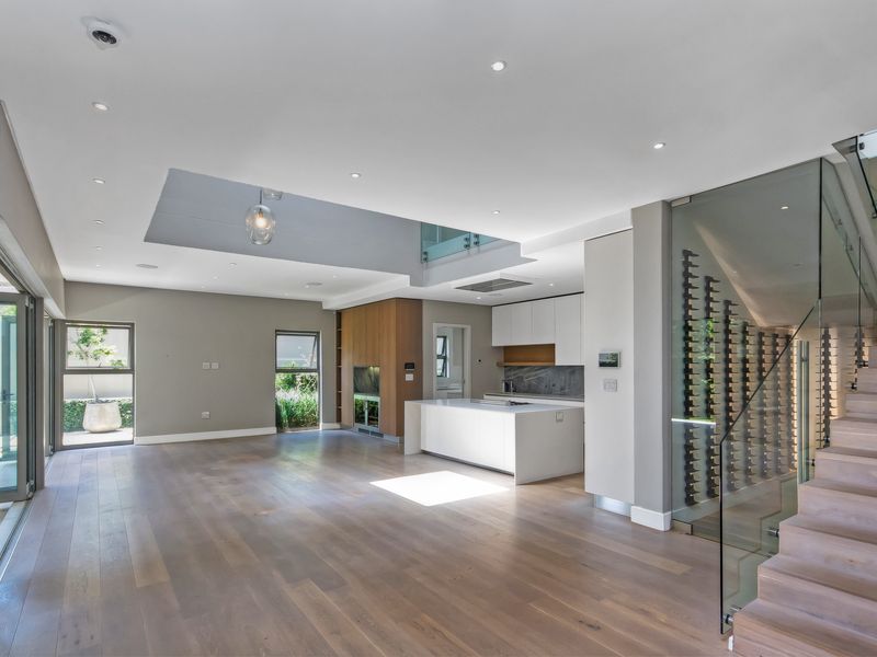 Spacious open-plan living area featuring hardwood floors, a modern kitchen with island, glass-enclosed wine display, and a staircase with glass balustrade.