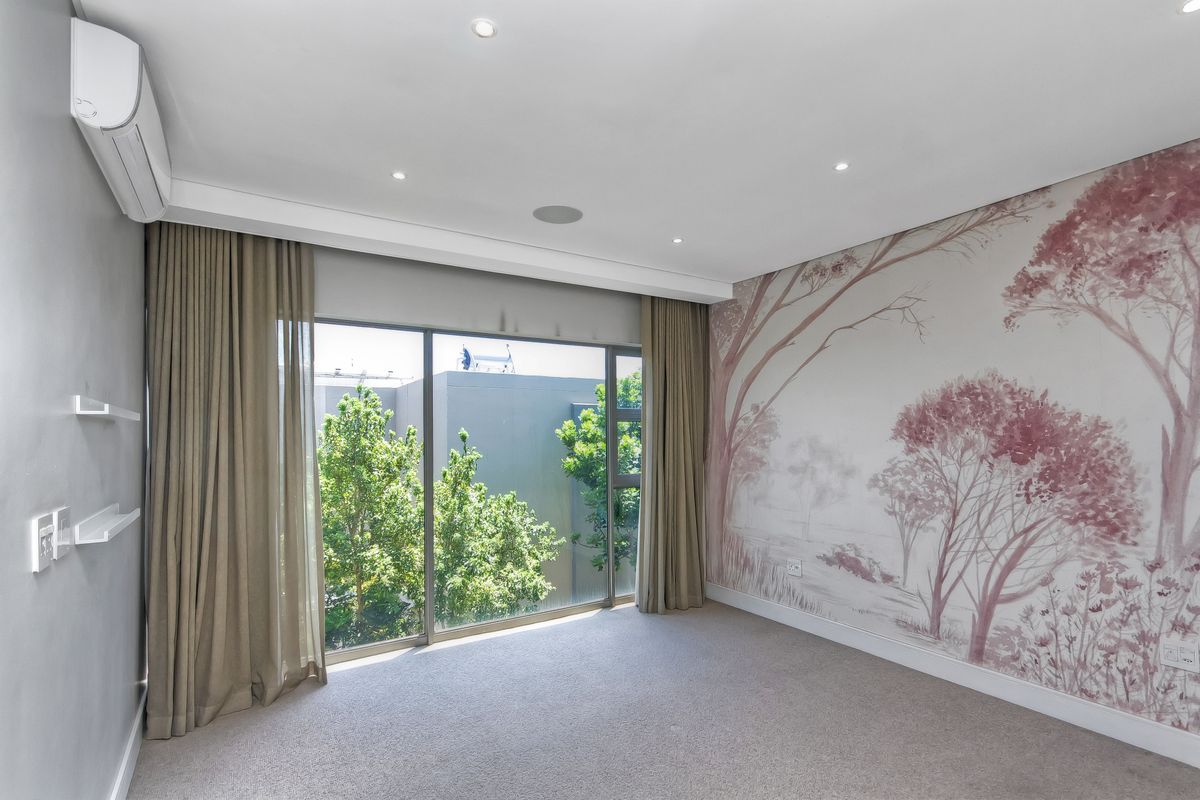 A bright, spacious bedroom featuring neutral carpeting, recessed lighting, an air conditioning unit, and a large sliding door with floor-to-ceiling curtains.