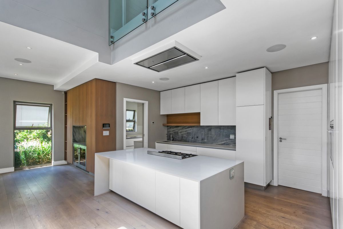 Modern open-plan kitchen featuring a central island with gas hob, sleek white cabinetry, stone countertops, and high-end integrated appliances in a bright, contemporary space.