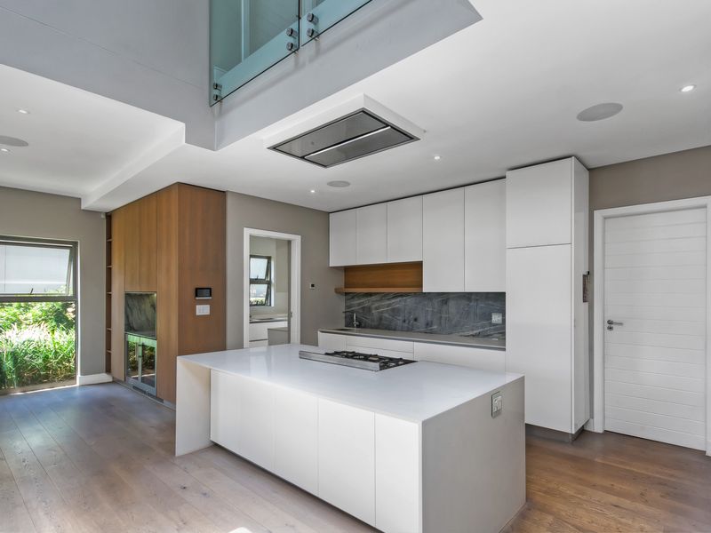 Modern open-plan kitchen featuring a central island with gas hob, sleek white cabinetry, stone countertops, and high-end integrated appliances in a bright, contemporary space.