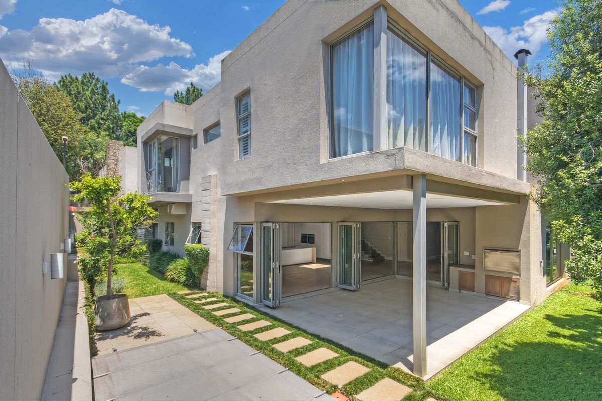 Rear view of a modern cluster home featuring a covered patio with built-in braai, stacking doors, and a well-maintained garden.