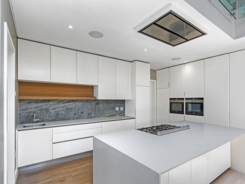 Modern kitchen featuring sleek white cabinetry, a central island with a gas hob, double wall ovens, and high-end stone finishes.