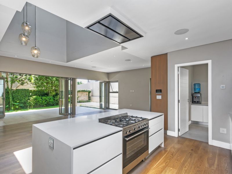 Modern open-plan kitchen featuring a central island with gas hob, sleek cabinetry, hardwood floors, and seamless access to the outdoor patio through stacking doors.