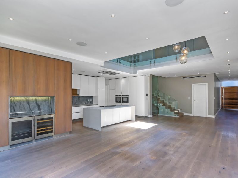 Spacious open-plan living and kitchen area featuring modern cabinetry, a central island, integrated appliances, and a striking glass-railed staircase.