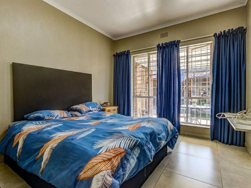 A bedroom featuring tiled flooring, security bars on the windows, and cove cornicing, offering a functional space with direct access to the exterior.