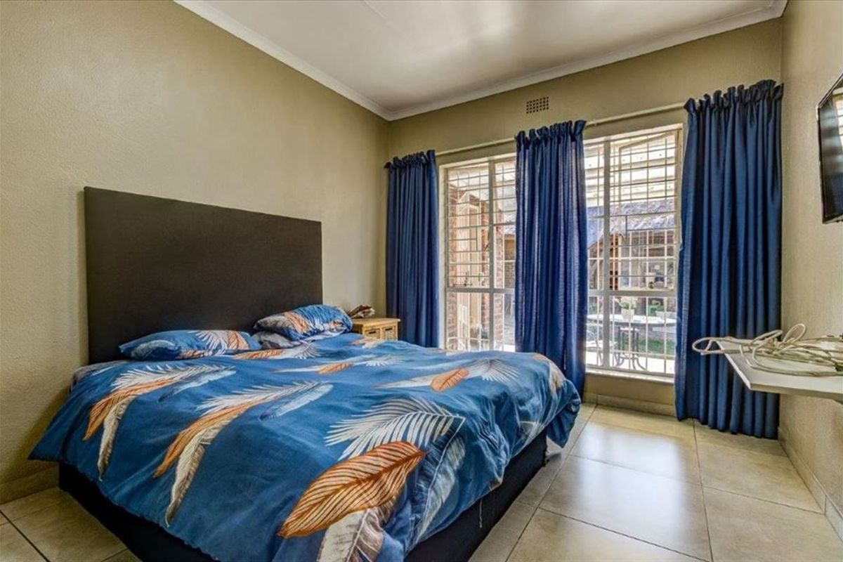 A bedroom featuring tiled flooring, security bars on the windows, and cove cornicing, offering a functional space with direct access to the exterior.