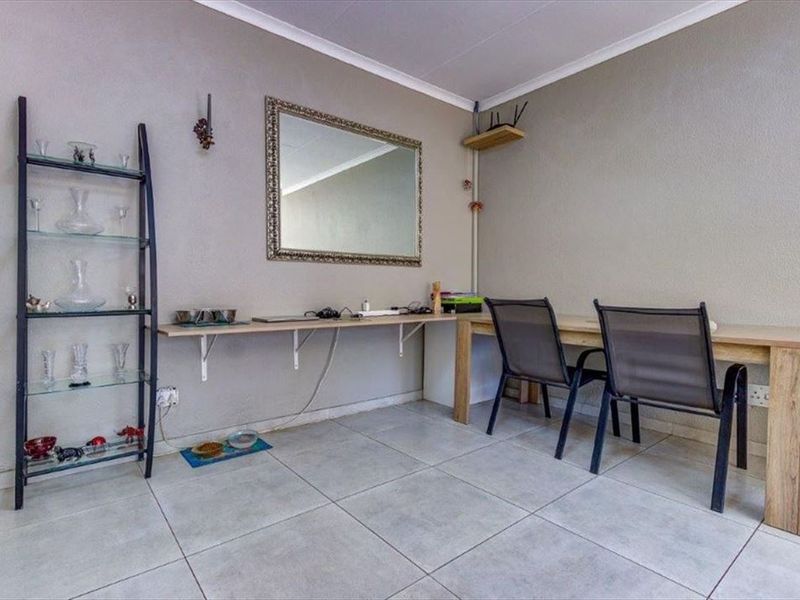 A functional living area featuring neutral tiled flooring, coved ceilings, and wall-mounted shelving, providing a versatile space for a home office or study nook.