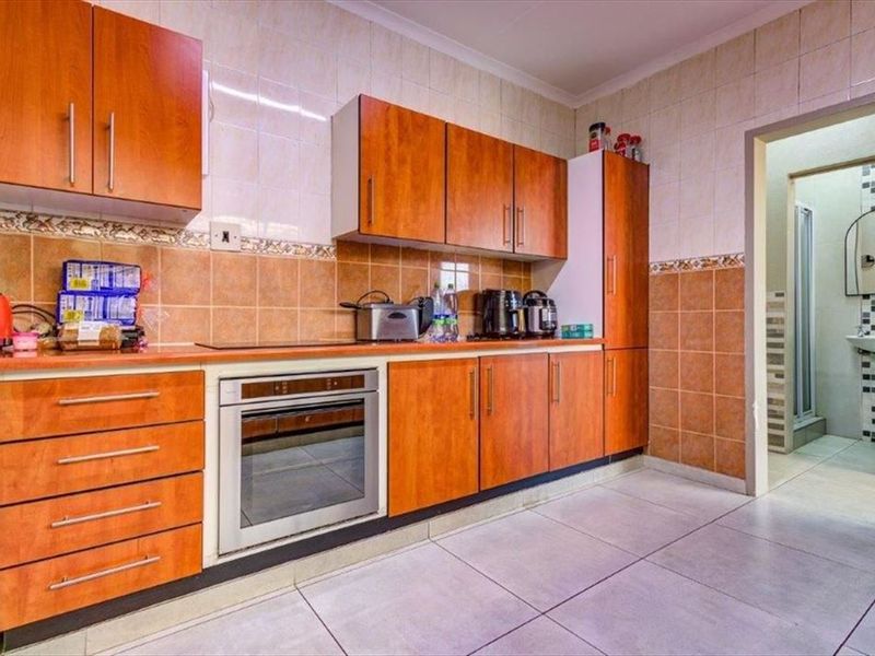A functional kitchen featuring wood-finish cabinetry, built-in oven, and tiled surfaces, with an adjacent doorway leading to a bathroom area.