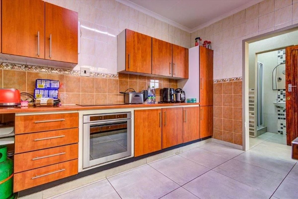 A functional kitchen featuring wood-finish cabinetry, built-in oven, and tiled surfaces, with an adjacent doorway leading to a bathroom area.