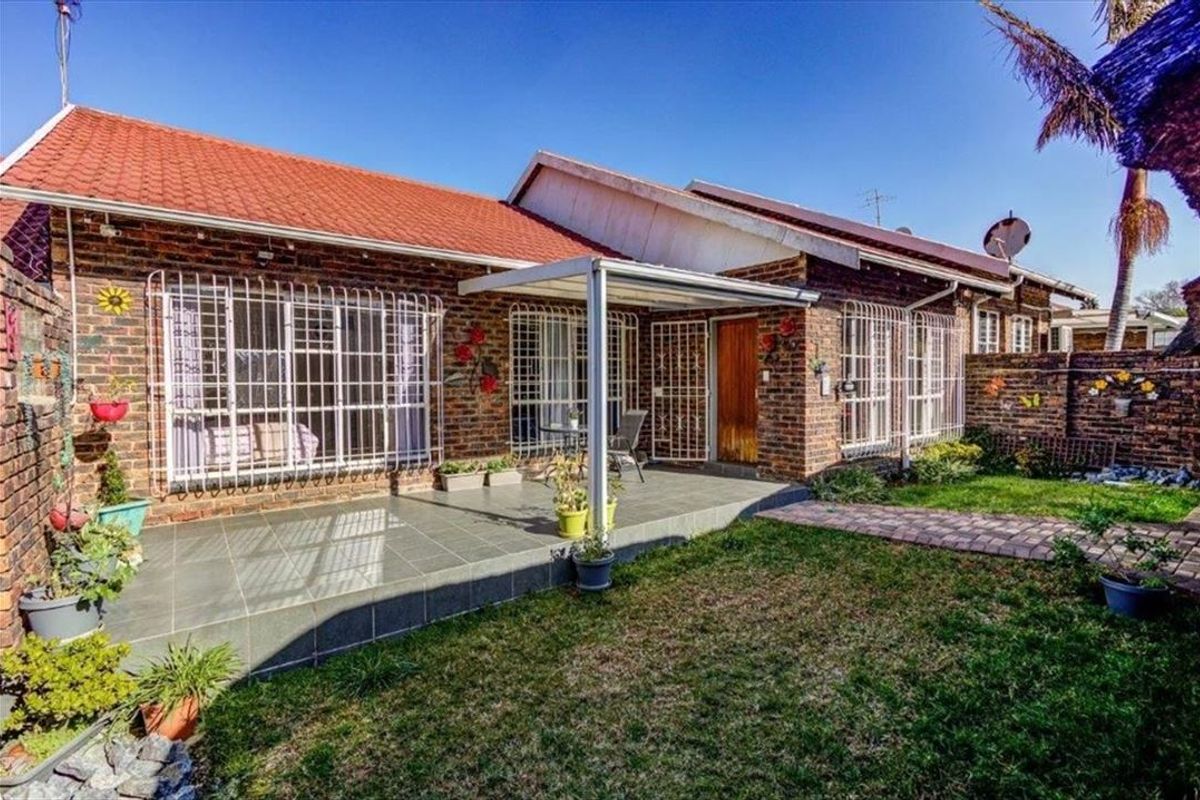 Rear view of the townhouse featuring a brick facade, a covered patio area, and a private garden with a paved walkway.